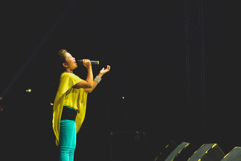Valokuva naisesta laulamassa mikrofoniin lavalla. Kuvan lähde: MD Duran, Unsplash. 